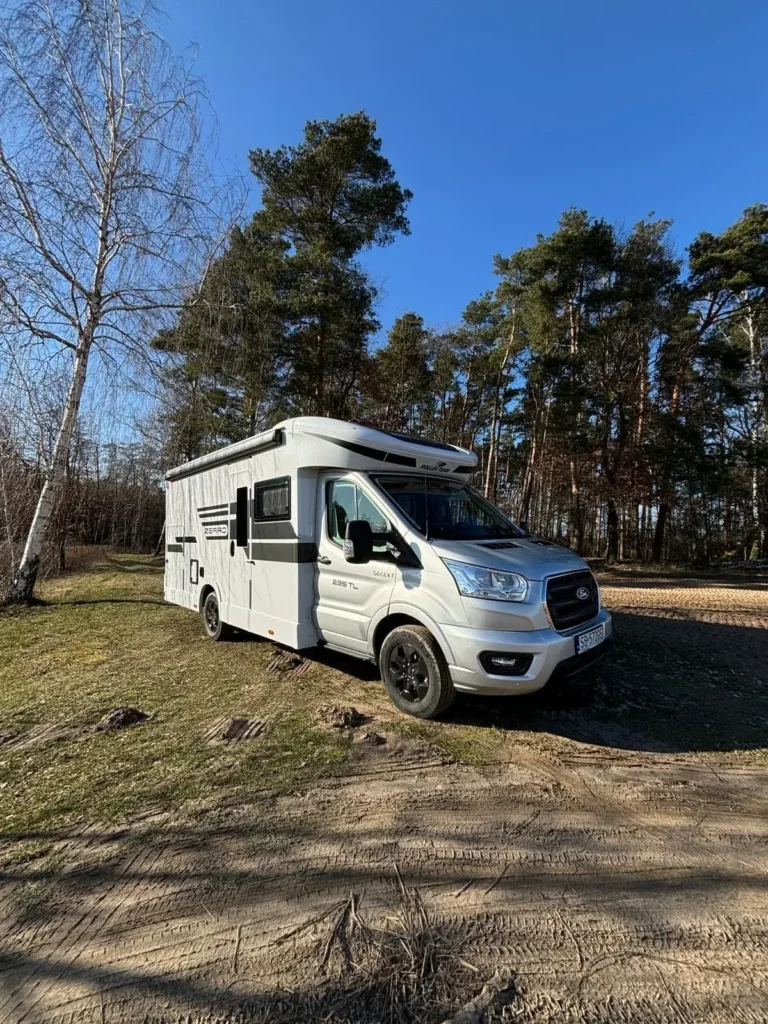 Roller Team Zefiro – kamper gotowy do podróży w otoczeniu natury Kamper Roller Team Zefiro zaparkowany przy lesie w słoneczny dzień, idealny na wyjazd z dala od miasta