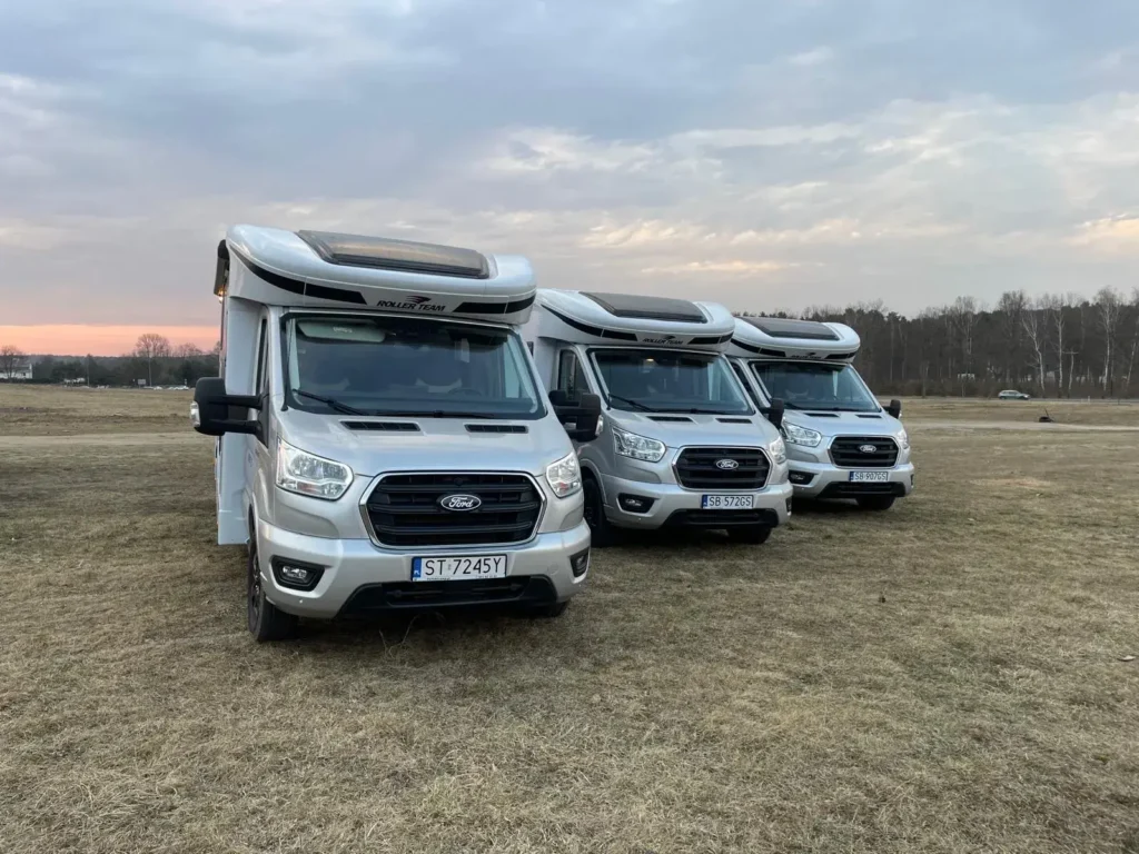 Kampery Roller Team Zefiro gotowe do podróży – zdjęcie z pola postojowego o zachodzie słońca Trzy kampery Roller Team Zefiro zaparkowane na otwartym terenie, gotowe do wynajmu