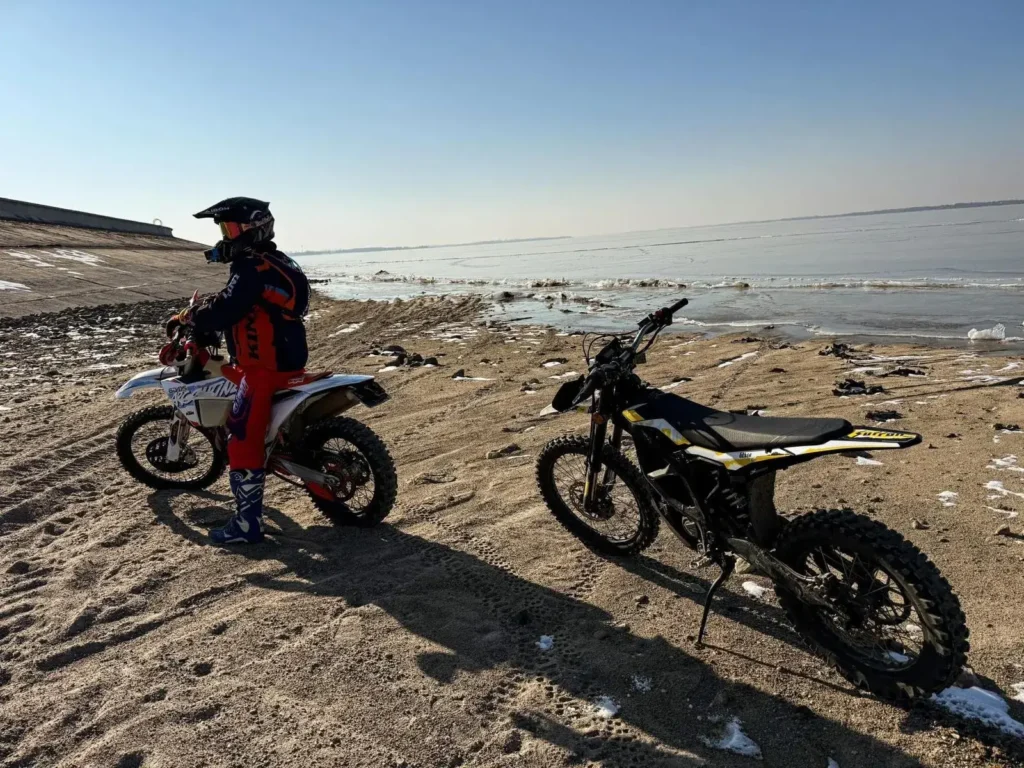 Elektryczny motocykl crossowy Surron Ultra Bee na piaszczystym brzegu – dodatkowa atrakcja do kampera